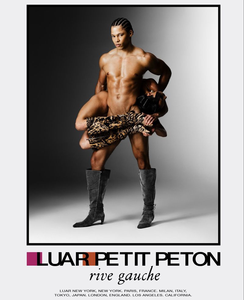 Two nude fashion models pose in studio, one supported by the other wearing long boots, with 'LUAR Petit Peton' logo below.