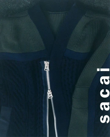 Close-up of a dark navy knit cardigan with olive green ribbed panels and a prominent silver two-way zipper.