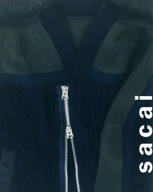 Close-up of a dark navy knit cardigan with olive green ribbed panels and a prominent silver two-way zipper.