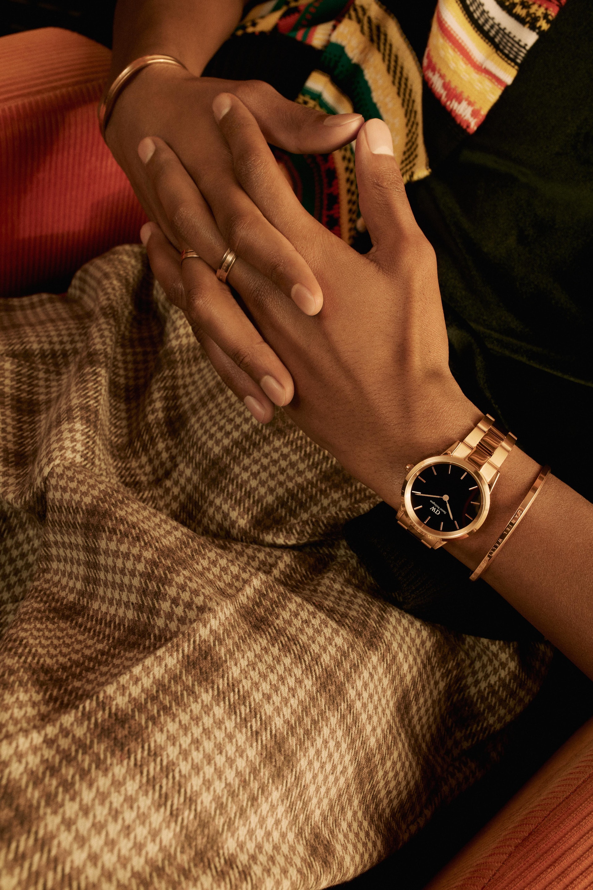 Close-up of two people holding hands, showcasing a wristwatch and jewelry against a patterned skirt, highlighting fashion accessories.
