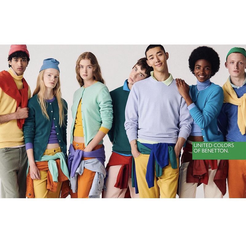 Diverse group of young adult fashion models in colorful knitwear by United Colors of Benetton posing against a neutral background.