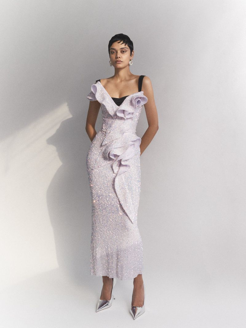 Elegant adult female in a shimmering lilac gown with silver heels, posing in a brightly lit studio setting with a neutral backdrop.