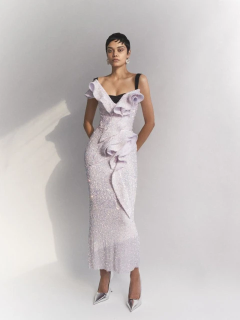 Elegant adult female in a shimmering lilac gown with silver heels, posing in a brightly lit studio setting with a neutral backdrop.