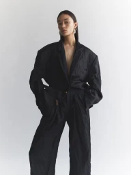 Model wearing an oversized dark blazer and matching trousers against a plain white studio background.