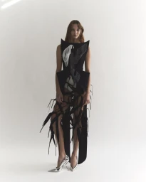 Model wearing a structured black sculptural dress and metallic pumps against a plain white background for Maticevski R25.