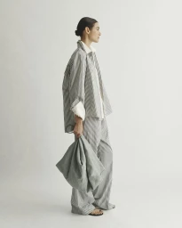Model wearing striped shirt and matching trousers holding a large grey handbag against a seamless white background.