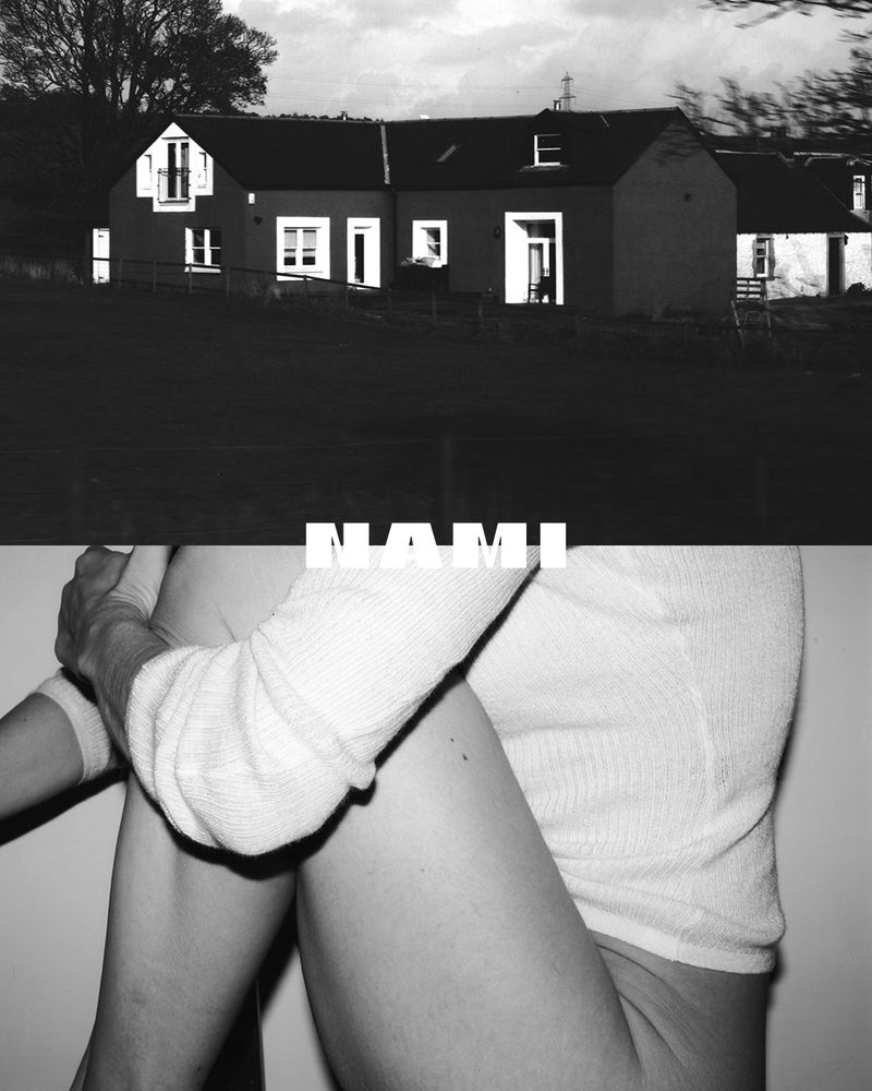 Monochromatic image showcases a building against a dark sky, juxtaposed with a person hugging their knees, creating a stark contrast.