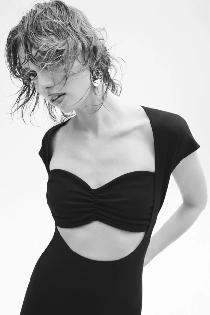 Monochrome portrait of a young adult woman with wet, short hair wearing a black dress in a photo studio with a plain white background.