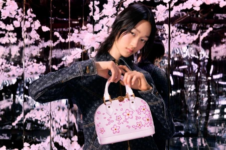 Model holding a pink cherry blossom handbag wearing a monogram denim jacket amidst blooming floral installations