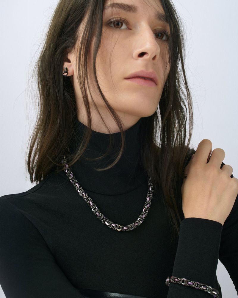 Portrait of a brunette adult female wearing a black turtleneck, silver chain necklace, silver earrings, and a silver bracelet.