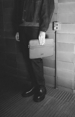 Person in denim jacket holding a laptop case against a tiled wall, creating a stylish and practical fashion product shot.