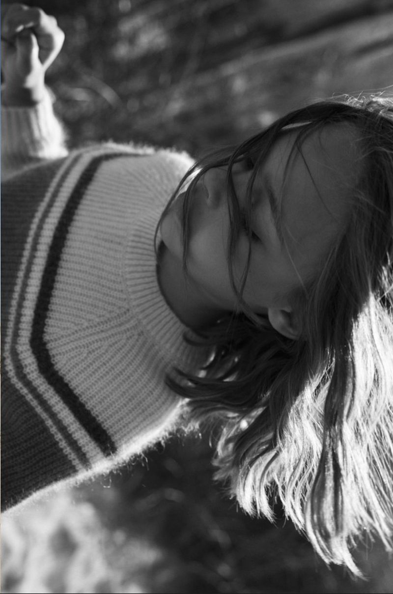 Close-up monochrome portrait of a child wearing a striped knit sweater with hair blowing across her face.