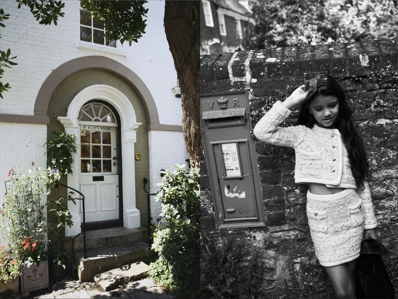 Young girl in tweed skirt suit poses next to a red post box in front of a stone wall outdoors in a vintage-style monochromatic fashion photograph.