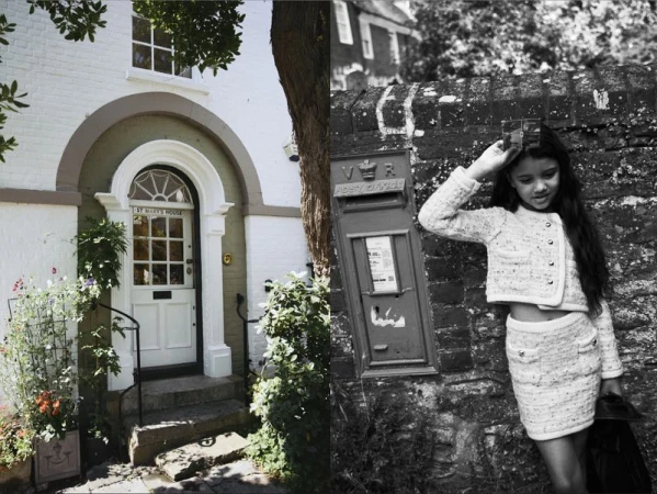 Young girl in tweed skirt suit poses next to a red post box in front of a stone wall outdoors in a vintage-style monochromatic fashion photograph.