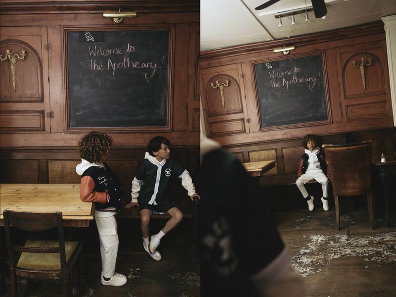 Two children in retro-style clothing in a room with wood paneling and a chalkboard sign that reads 'Welcome to The Apothecary'.