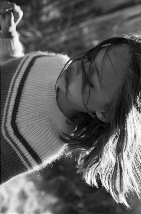 Close-up monochrome portrait of a child wearing a striped knit sweater with hair blowing across her face.