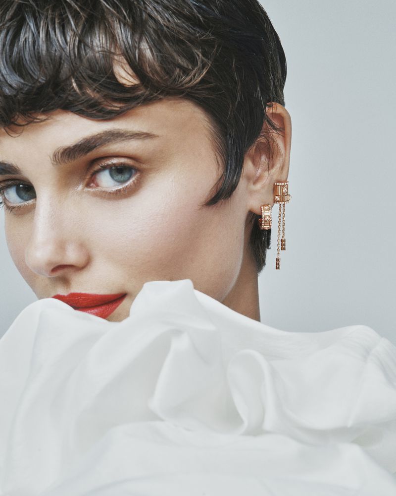 Close-up portrait of a woman with short dark hair wearing gold earrings and red lipstick behind white fabric