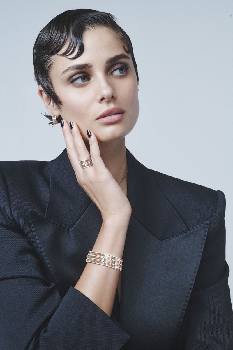 Elegant woman in a black blazer with stylish short hair and jewelry posing in front of a white background for a beauty concept shoot.