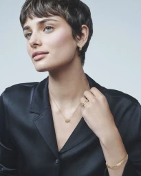Taylor Hill wearing gold jewellery and a black silk shirt against a seamless light background for Life by Marli.