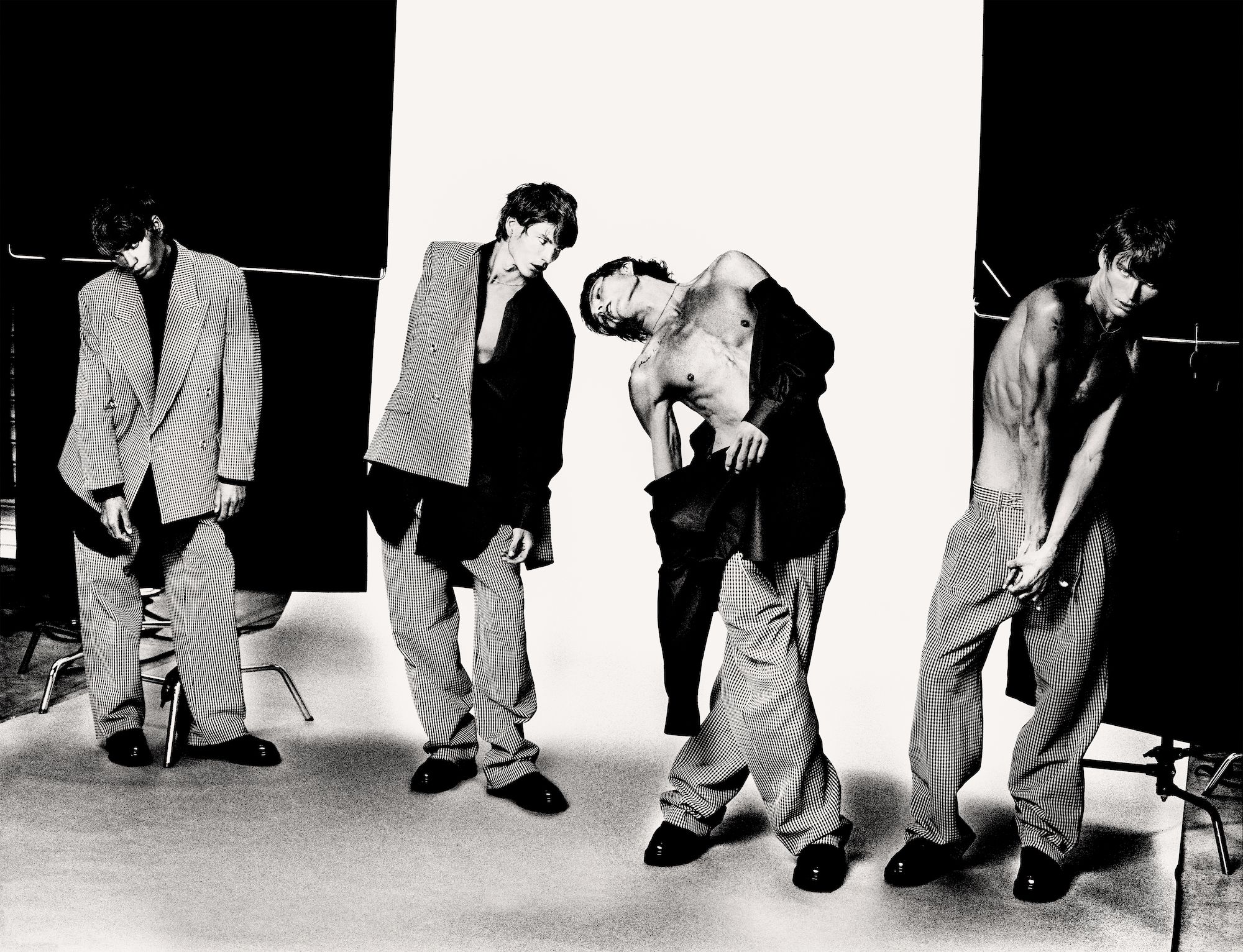 Black and white fashion studio shot of four young adult men posing in loose suits with trousers and a black and white studio backdrop.