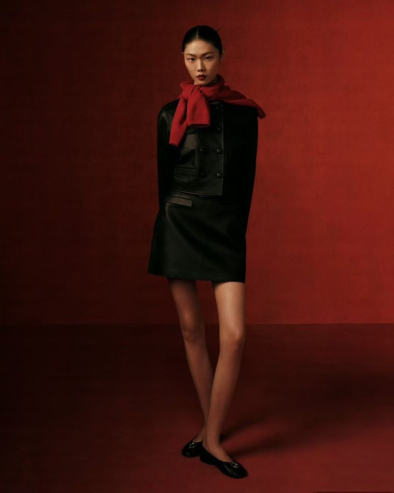 Asian woman in dark jacket and skirt posing in photo studio with dark red background and floor. Red scarf for accent. Fashion shot.