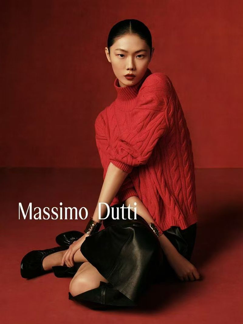 Fashion portrait of an Asian model in a red knit sweater and black skirt, kneeling against a red background, with the Massimo Dutti logo.