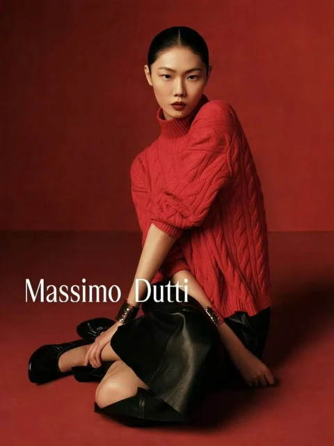 Fashion portrait of an Asian model in a red knit sweater and black skirt, kneeling against a red background, with the Massimo Dutti logo.
