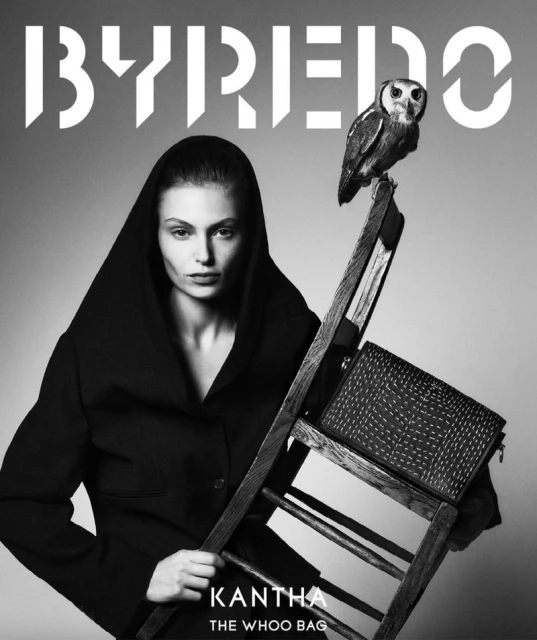 Black-and-white fashion ad featuring a woman in a hooded coat, an owl perched on a wooden ladder, and a stylish purse.