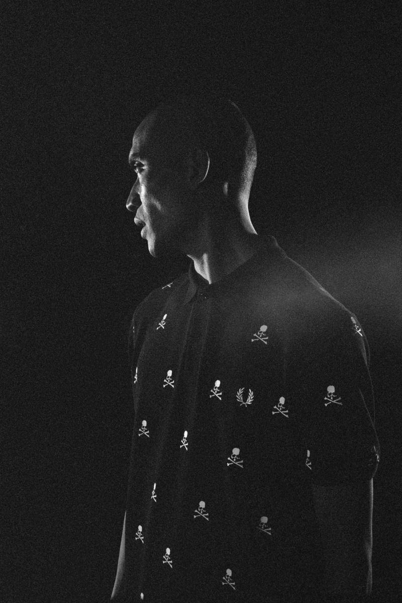 Black and white portrait of an adult male in a skull-patterned polo shirt, gazing to the side against a dark background.