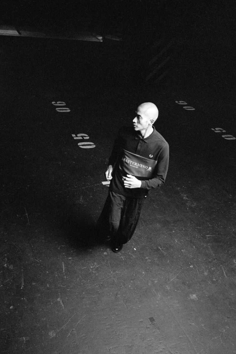 Monochrome portrait of a bald adult man in a polo shirt and dark pants, captured in an overhead, high-angle shot with dramatic lighting.