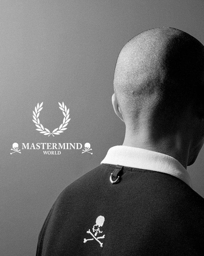 Back view of a person wearing a polo shirt with skull embroidery, featuring the Mastermind World logo and white collar against a gray backdrop.