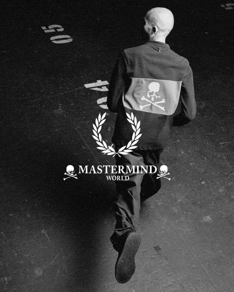 Rear view of a person in black clothing walking on a black floor with visible text and a logo featuring a skull and crossbones.