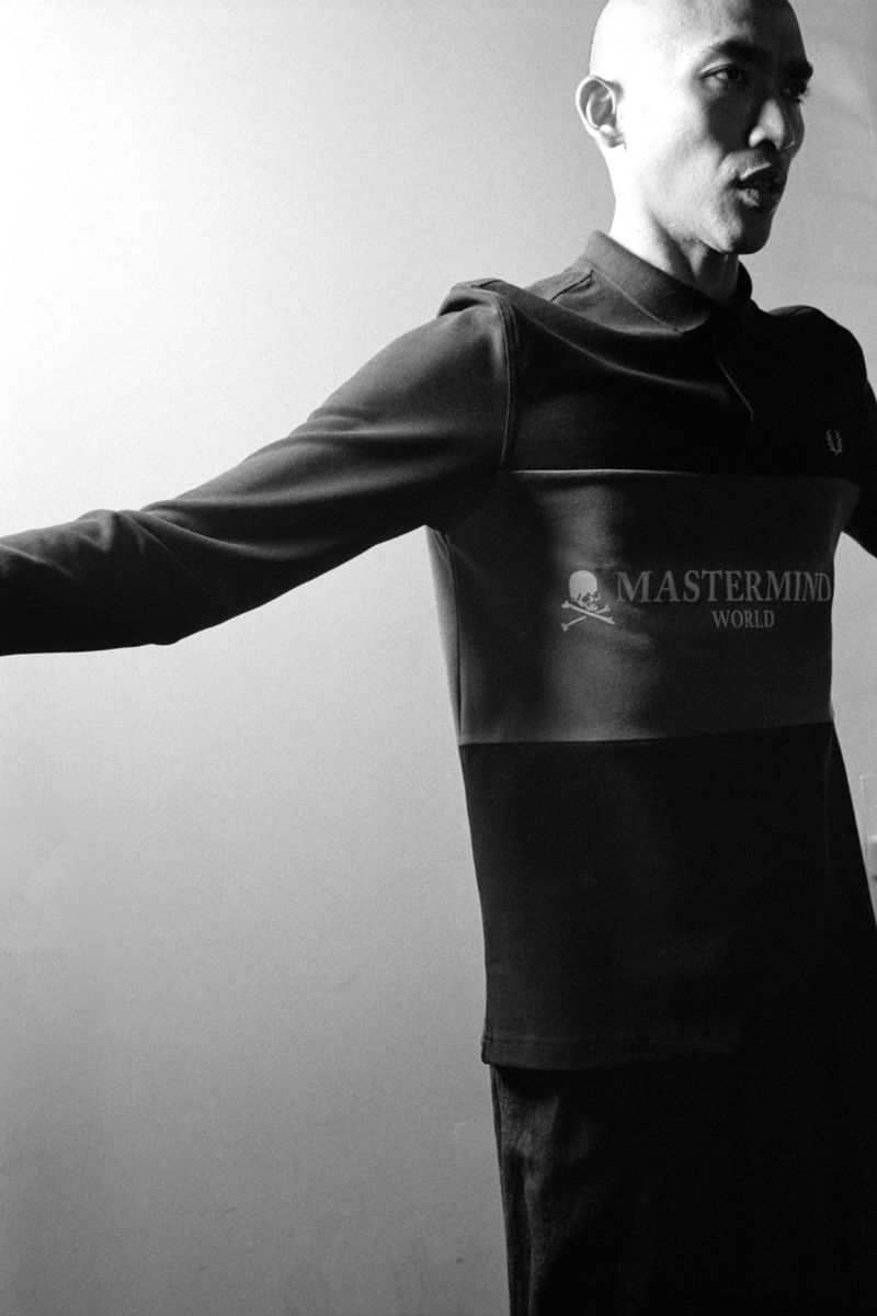 Black and white portrait of a bald adult male wearing a long-sleeved polo shirt with the Mastermind World logo, against a plain backdrop.