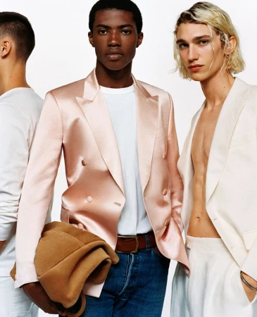 Three men wearing satin and linen blazers pose in a fashion shot. One is holding a brown jacket in his arm. They are on white background.