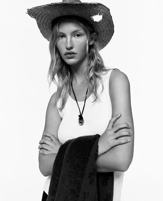 Model wearing a straw hat and white tank top holding a towel against a white background for the Fursac S/S 2025 campaign.