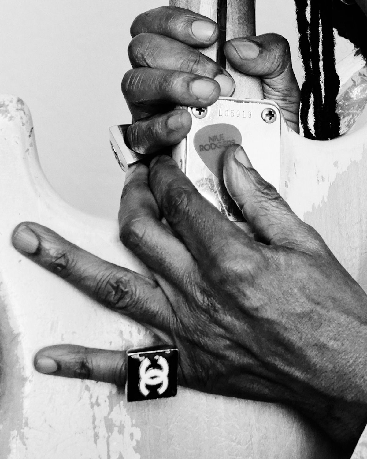 Close-up black and white shot featuring an adult's hands adorned with rings holding a guitar neck, showcasing jewelry and musical instrument.
