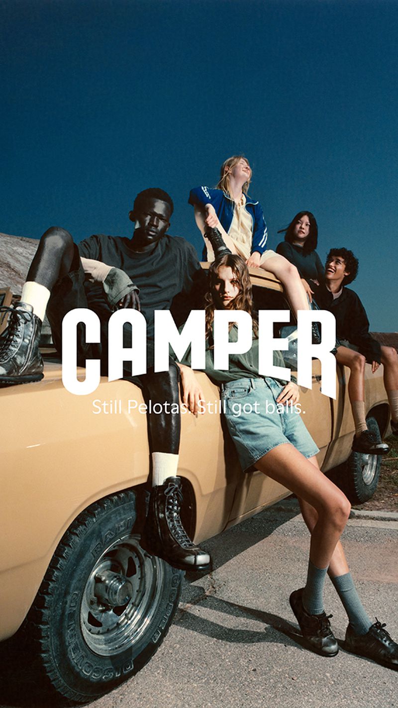 Diverse group of young adult friends pose on a vintage yellow car with a bright blue sky, showcasing relaxed fashion and camaraderie.