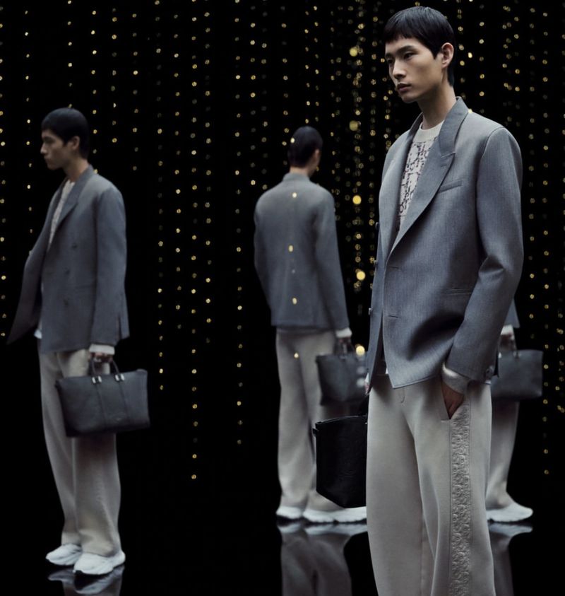 Asian male fashion model posing in a gray suit with black leather briefcase, and a black and gold bokeh background. Studio lighting.