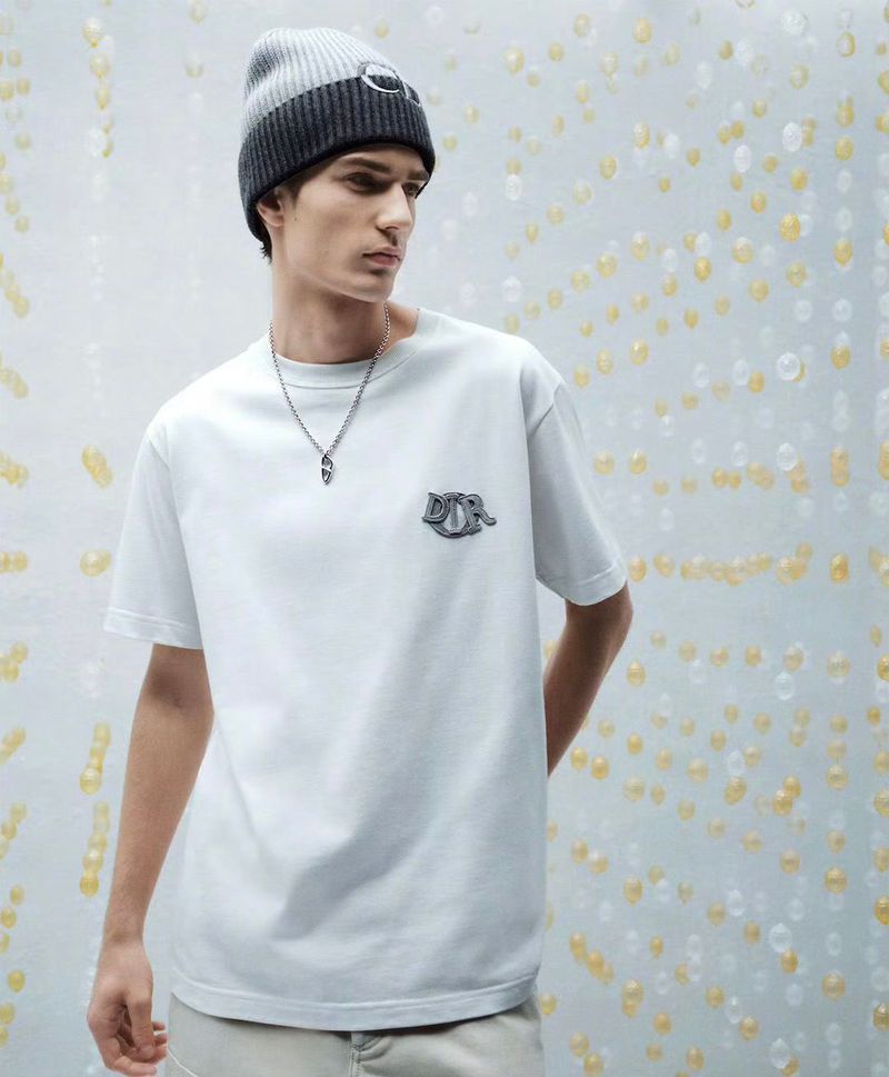 Man wearing a white t-shirt with the Dior logo and a gray and white beanie poses against a textured background of round shapes.