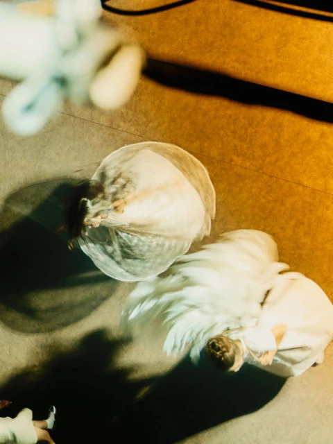 An eye-level shot shows blurry figures in motion on a gold-toned surface, creating a dreamlike effect, with shadows and undefined details.