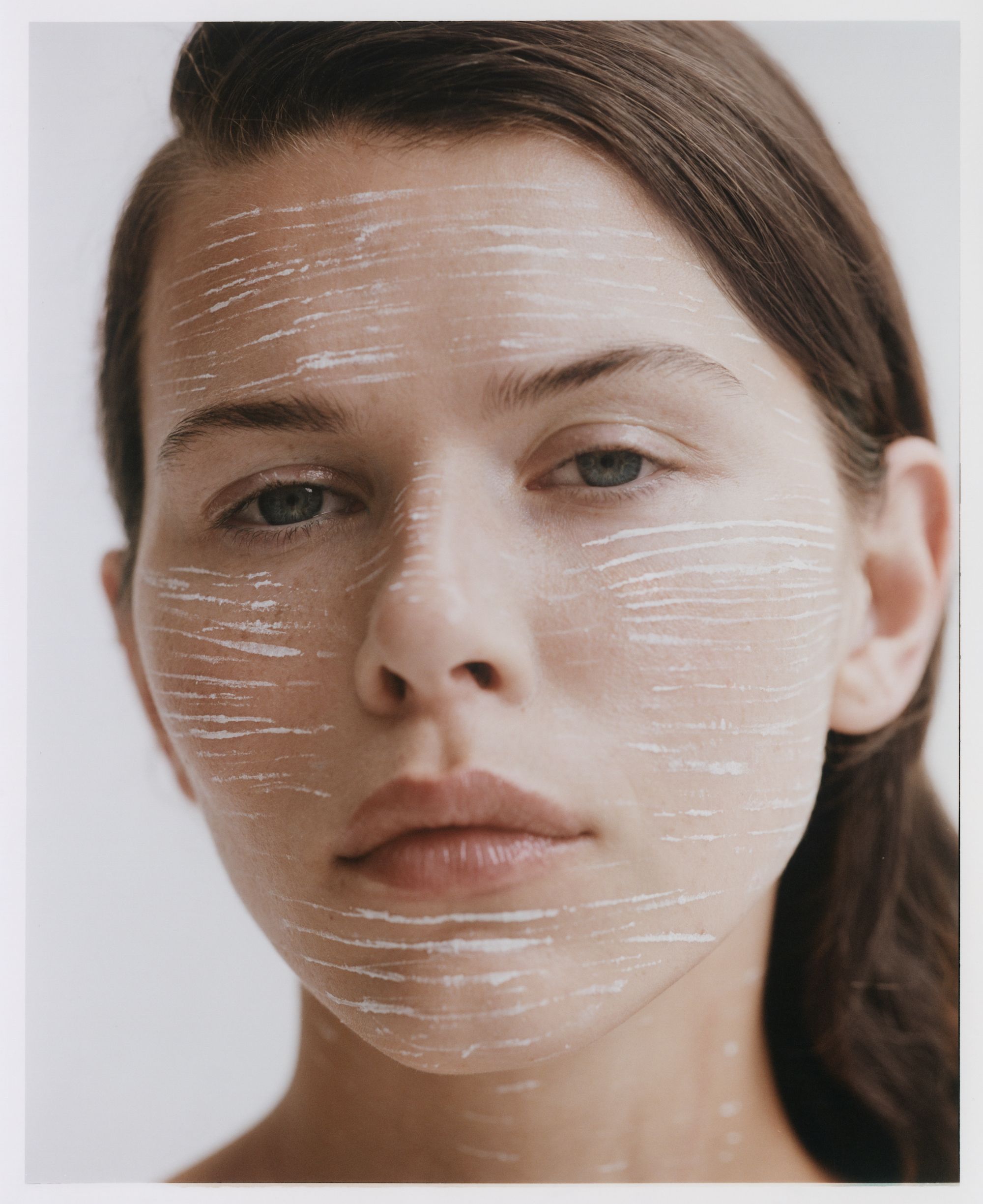 Close-up portrait of a woman with white cosmetic streaks across her face for Russh magazine by Justin Woo