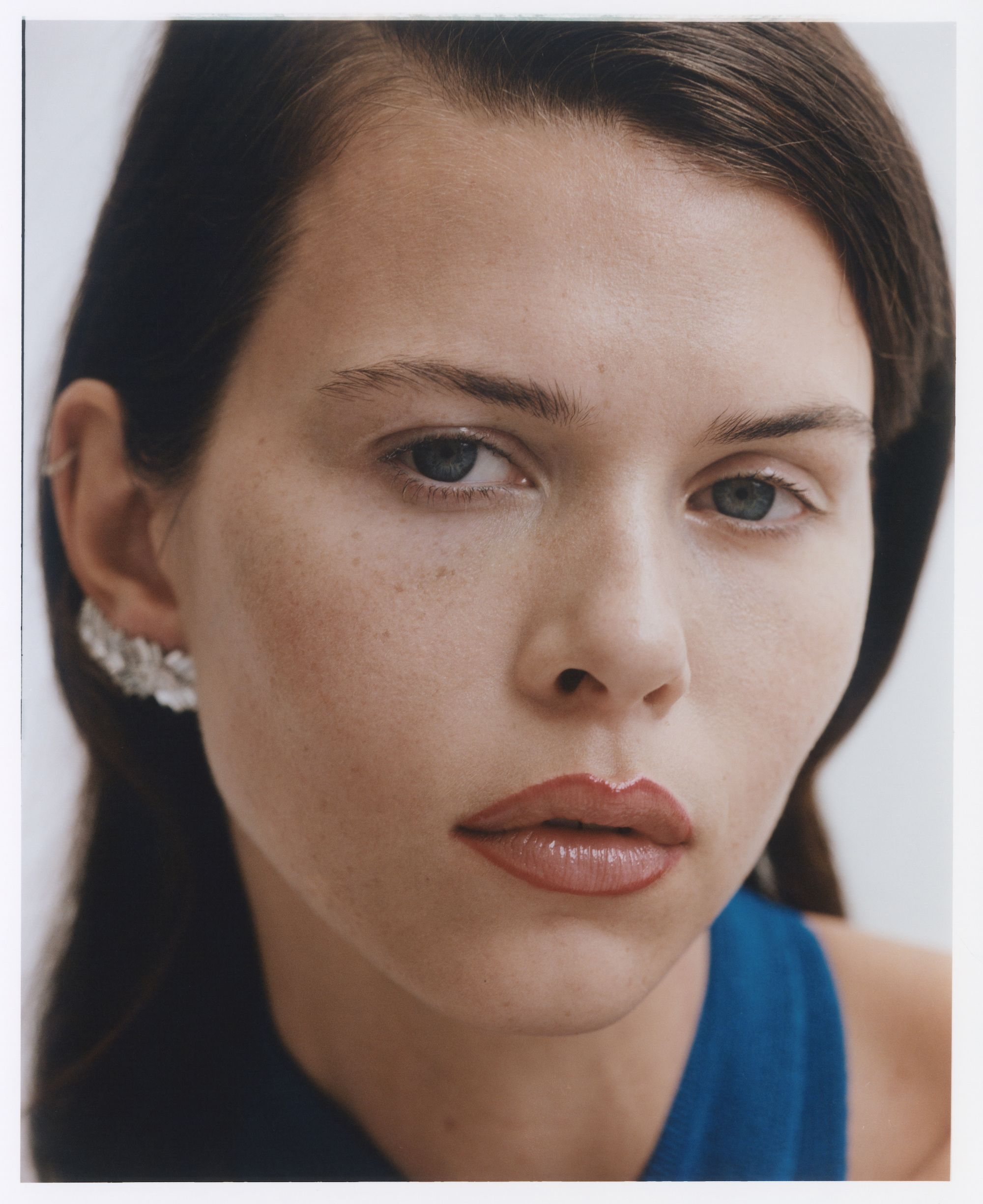 Close-up portrait of a woman with dark hair wearing a blue top and crystal ear cuff against a plain white background