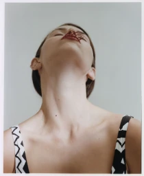 Low angle portrait of a woman wearing a black and white patterned top with red objects placed on her lips.