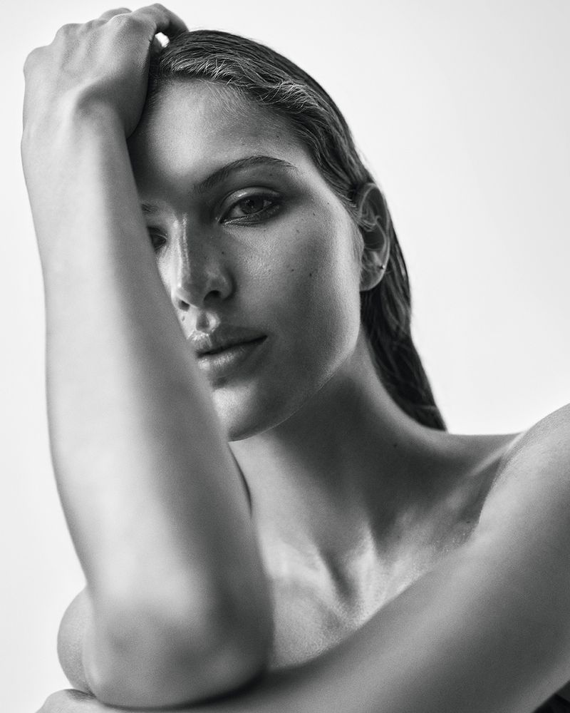 Monochrome portrait of a woman with wet hair, posing with a hand on her head in a studio setting against a white background.