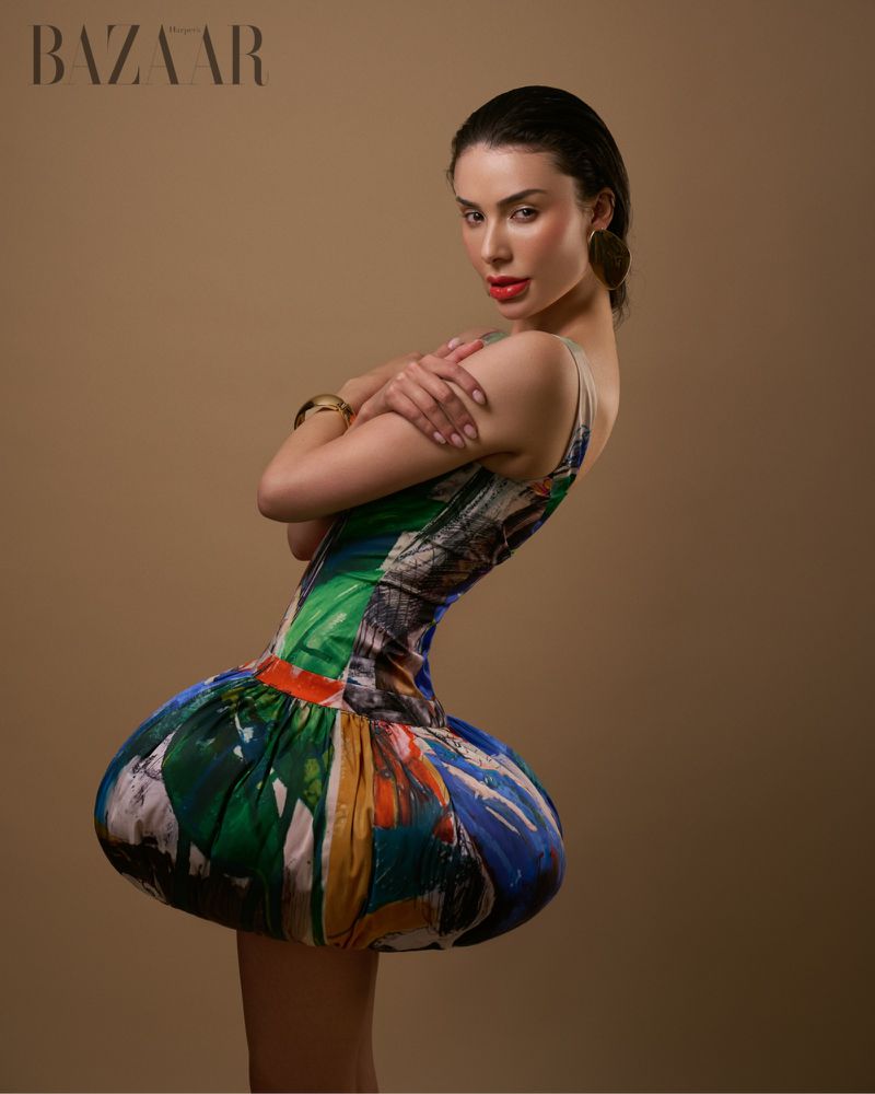Brunette woman in avant-garde colorful short dress with arms crossed in a studio setting for fashion editorial shot.