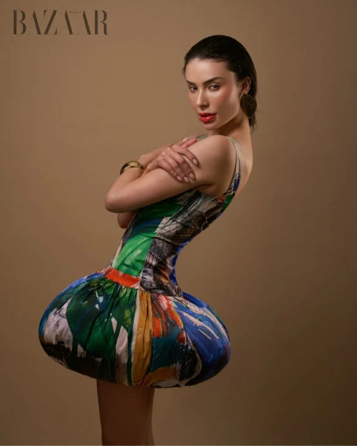 Brunette woman in avant-garde colorful short dress with arms crossed in a studio setting for fashion editorial shot.