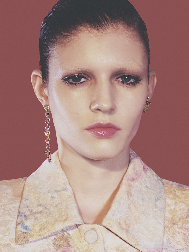 Close-up portrait of model Camille Chifflot with slicked-back hair and dangling gemstone earrings for Crash Magazine