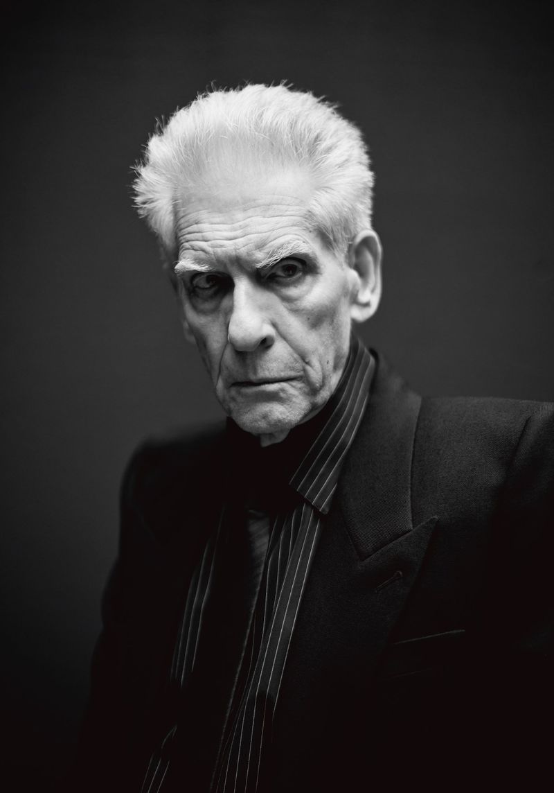Portrait of David Cronenberg wearing a dark striped suit jacket against a dark background for Crash Magazine.