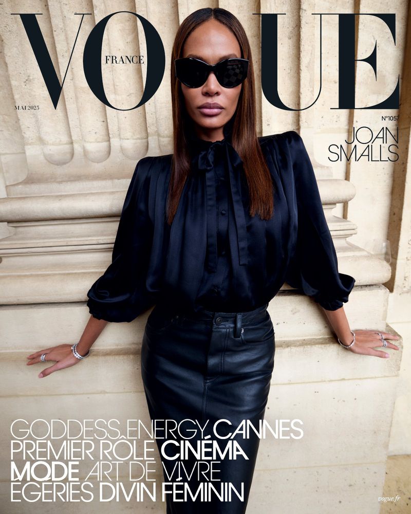 Vogue France cover featuring Joan Smalls in a black satin blouse and leather skirt, accessorized with sunglasses and jewelry, against an architectural backdrop.