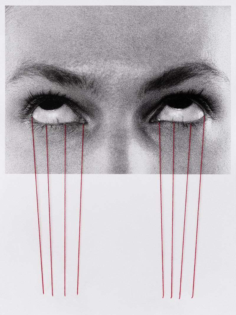 Close-up artistic black and white image of a person's eyes with red thread running down from the eyes on a white background.